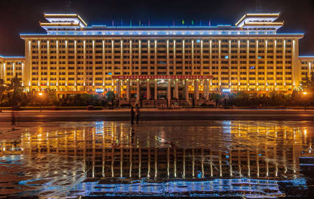 Xian, China - May 1, 2010: Black night landscape closeup. Lighted up Shaanxi Peoples Government Office Building with people up front. Reflection in wet surface.のeditorial素材