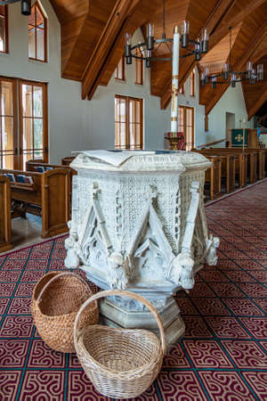 Los Olivos, California, USA - September 3, 2020: Closeup of white stone decorated baptismal font at St. Marks in the Valley Church with brown wooden ceiling and benches behind.のeditorial素材