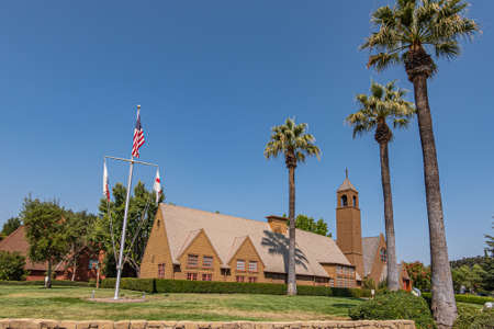 Los Olivos, California, USA - September 3, 2020: Wide view on brown wood St. Marks in the Valley Church with bell tower set in green park under blue sky, including side buildings. Flag post up front.のeditorial素材