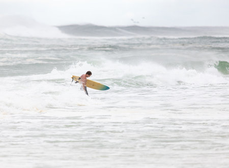 Surfer heads back to shore with large waves crashing in the background