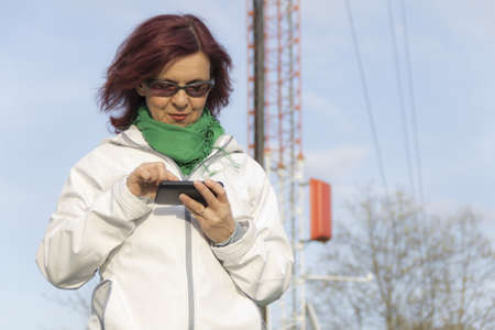 Good looking mid age woman with tablet phone under big antenna tower