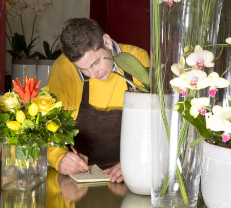 Florist accepting phone order from a customer in his flower shopの写真素材
