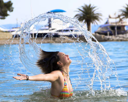 Cute young girl splashing out of the water on the beachの写真素材