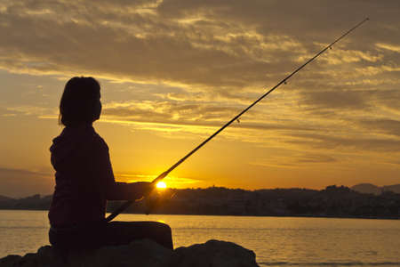 Happy girl fishes at sunset, near the sea at sunsetの写真素材