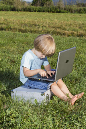Young boy typing on notebook, sitting on the grassの写真素材