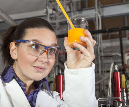 Closeup of a cute smiling female researcher holding test beaker and tube with chemicals, while...