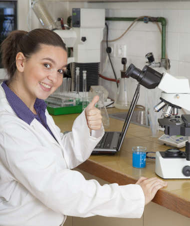Closeup of a cute female researcher showing OK sign, while carrying out some experiments in a...