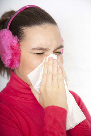 Cute young woman with earmuffs, who has caught cold, using handkerchief, whilst sneezingの写真素材