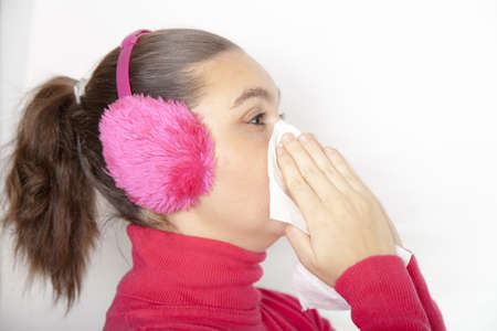 Cute young woman with earmuffs, who has caught cold, using handkerchief, whilst sneezingの写真素材