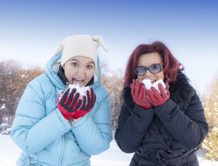 Cute mother and her smiling daughter eating snow  on sunny winter dayの写真素材