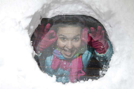 Cute smiling girl looking  through a hole in a snowy car window
