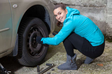 Changing tires, Young woman loosening nuts on a car wheel の写真素材