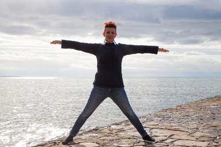 Cute middle aged  woman in casual clothing  at the seaside meditating and performing Yoga against...