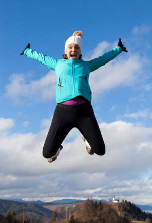 Young sportive women joyfully jumping in the mountains, with blue cloudy sky and small church in...