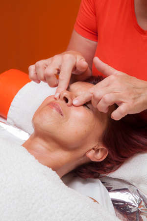 Cute mid aged woman receiving a professional therapeutic facial massage and lymphatic drainage, while lying on a towel in a award-winning health massage center, series of various techniques の写真素材