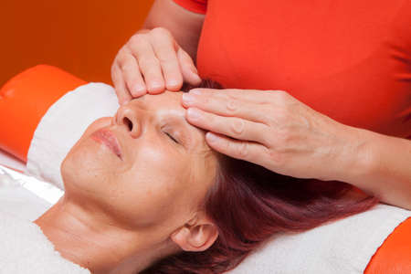 Cute mid aged woman receiving a professional therapeutic facial massage and lymphatic drainage, while lying on a towel in a award-winning health massage center, series of various techniques の写真素材