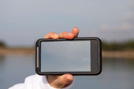 Hand showing smart mobile phone with blank screen, beach backgroundの写真素材