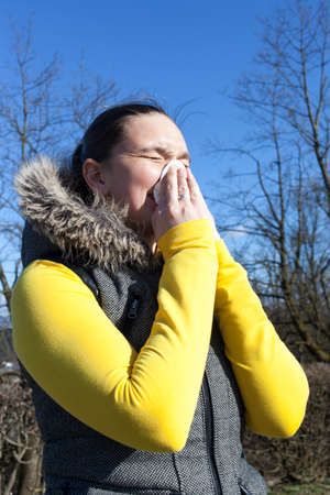 Pretty girl sneezing outdoors, on sunny windy day, against beautifull blue skyの写真素材