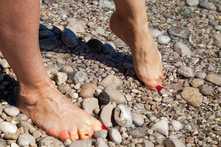 Close up on female legs walking and splashing water, on sand beach, against blue sea and sky, selective focus on legsの写真素材