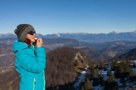 Pretty mid aged woman trekker woman putting balsam lips to repair her lips of the causes of winter...