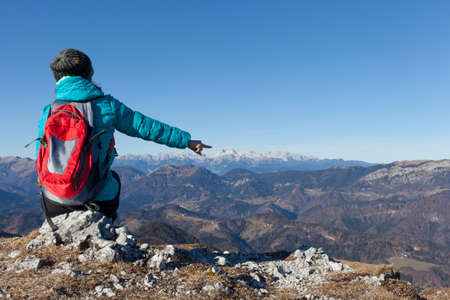 Trekker with backpack resting high in mountains on sunny winter day and pointing on Mount Triglav, highest mountain in Slovenian  Alps, space for textの写真素材