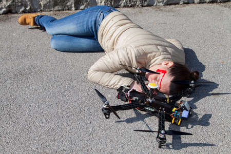 Pretty woman attacked by drone quadrocopter with bleeding head injuries,  lying on sidewalk in the city, space for textの写真素材
