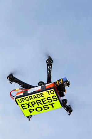 UAV drone quadrocopter with modern GPS navigation transporting inscription UPGRADE TO EXPRES POST against blue sky, space for textの写真素材