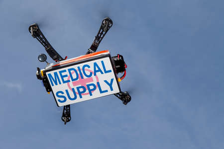 UAV drone quadrocopter with modern GPS navigation transporting box with medical supplies, against blue sky, space for textの写真素材