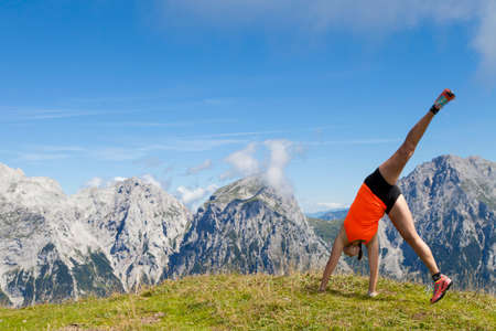 Young pretty women joyfully jumping and performing cartwheel, outdoors high in the mountains, on sunny summer dayの写真素材