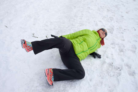 Risk of accidents in winter. Mid aged woman is slipping and falling on footpath, street covered with snow and black iceの写真素材