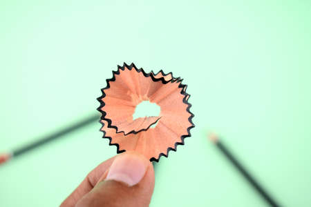 a person is holding a single piece of pencil shaving with a blurred background which have two black...