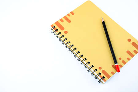 A dark black pencil on a designed orange notebook with a isolated whiteの写真素材