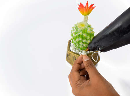 A person attaching a white stone to a miniature green tree with a black glue gun