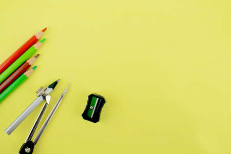 Study materials containing four different colored pencil crayons,a pencil attached to a pencil compass and a black pencil sharpener scattered on a yellow backgroundの写真素材
