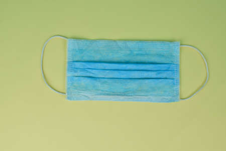 Blue surgical mask with rubber straps isolated on a light yellow paper backgroundの写真素材