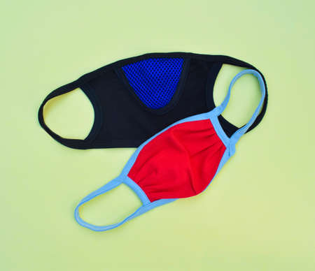 Two used facial mask of different color scattered on an isolated light yellow background