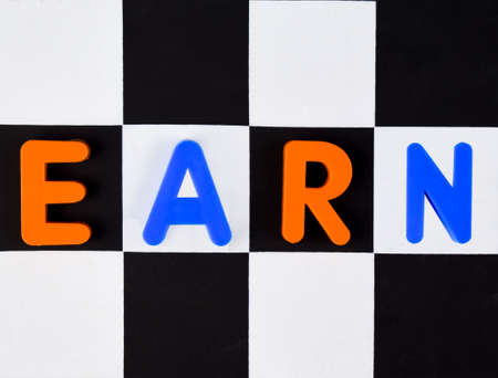 Earn word written with different colored letter blocks arranged on a black and white backgroundの写真素材