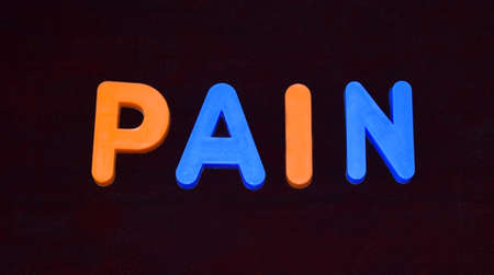 Pain word written with different colored letter blocks arranged on a dark backgroundの写真素材