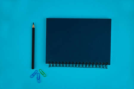 Three different colored paper clips,a black pencil crayon,and a diary on a blue paper background