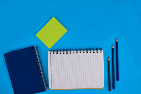 Three wood pencil crayons two diaries and some green sticky notes on a light blue paper background