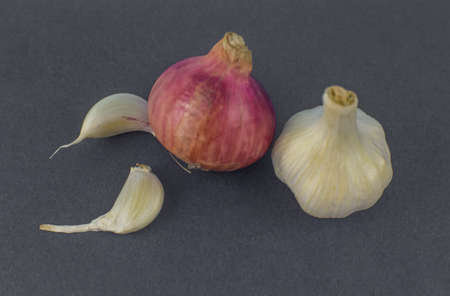 Pink colored medium size onion and a white garlic beside some garlic seeds before a dark background
