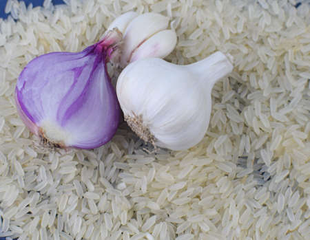 White colored garlic and a garlic seed placed beside a pink colored onion before stack of riceの写真素材