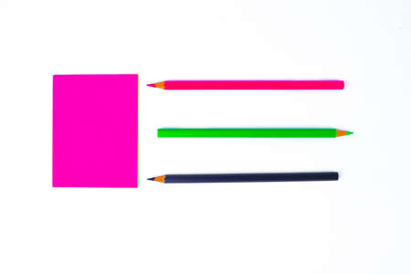 Top view of three different colored wood pencil crayons pointing at a pink sticky paper note