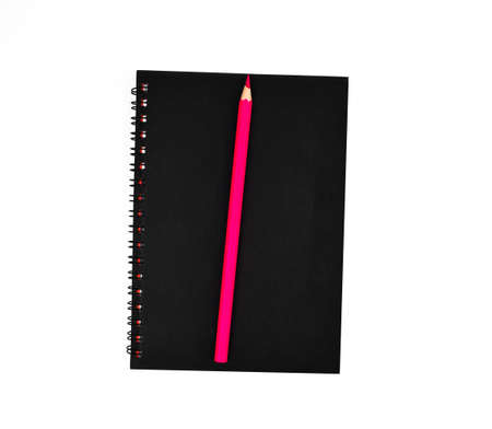 Pink pencil on top of a black color covered single note paper diary isolated on an empty white...