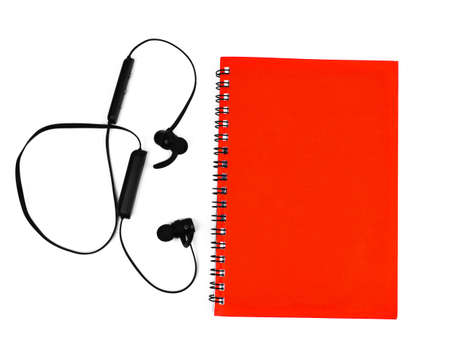 One black colored ear phone placed beside a single red colored note paper diaries before a white backgroundの写真素材