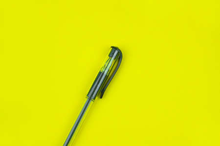 Black colored ball point pen placed over a bright yellow colored empty paper backgroundの写真素材