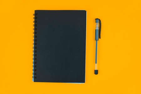 Study material containing a black paper diary and a black ball point pen placed on an orange paper...