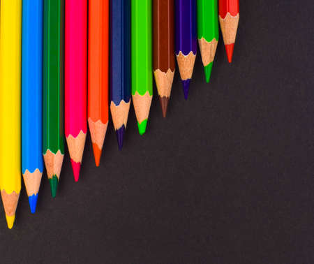 Waved row of different colored pencil crayon placed on top of an empty black colored paper backgroundの写真素材