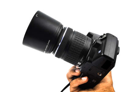 A person showing a black colored digital camera with a lens attached to it before a white background