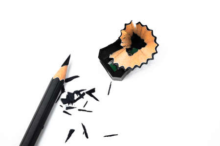 Black color wood pencil crayon placed beside a pencil sharpener and some fresh shavings
